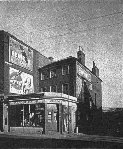 3 storey brick built property set back from the road with 'Meadow Dairy' corner shop to its front