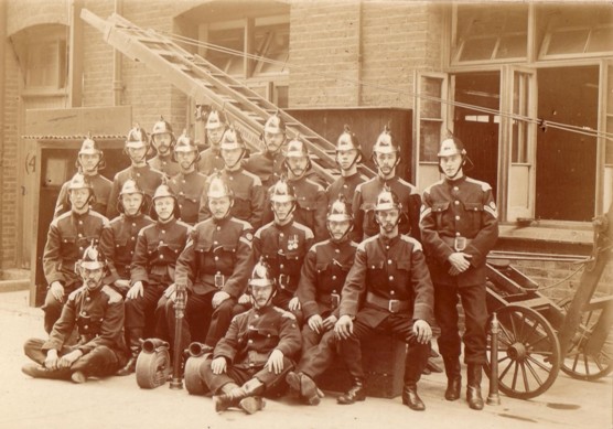 Sepia group photo of 20 firemen in uniform outside premises