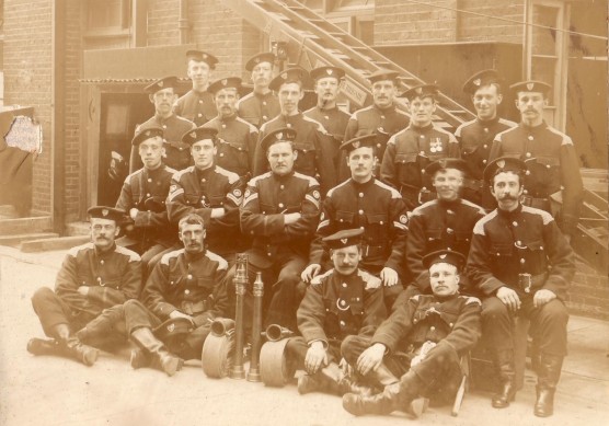 Sepia group photo of 20 firemen in uniform outside premises