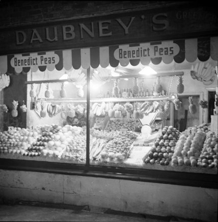 B/W photo taken in evening, showing greengrocers shop display